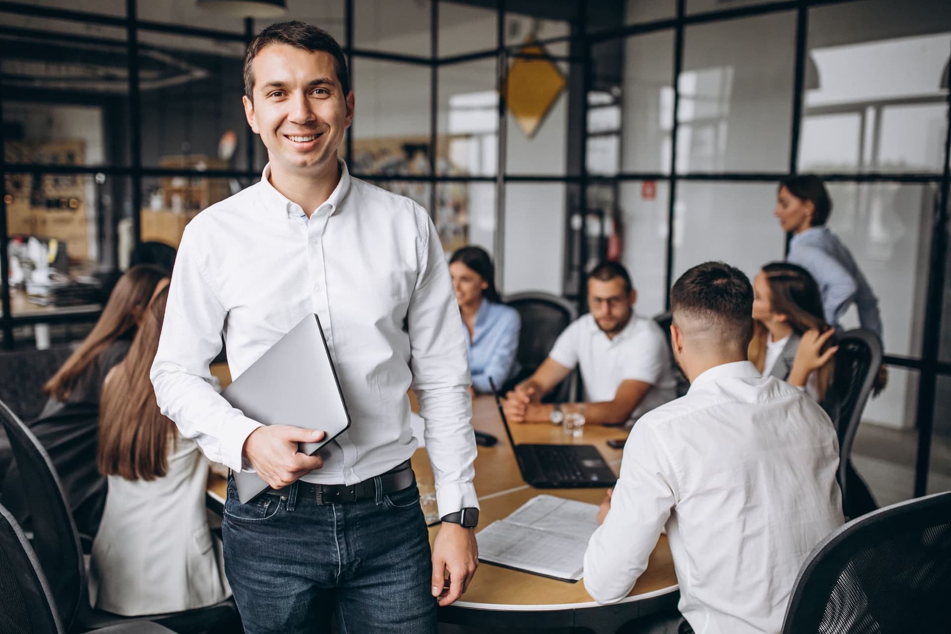 Gestor sorrindo em ambiente de trabalho com a equipe ao fundo