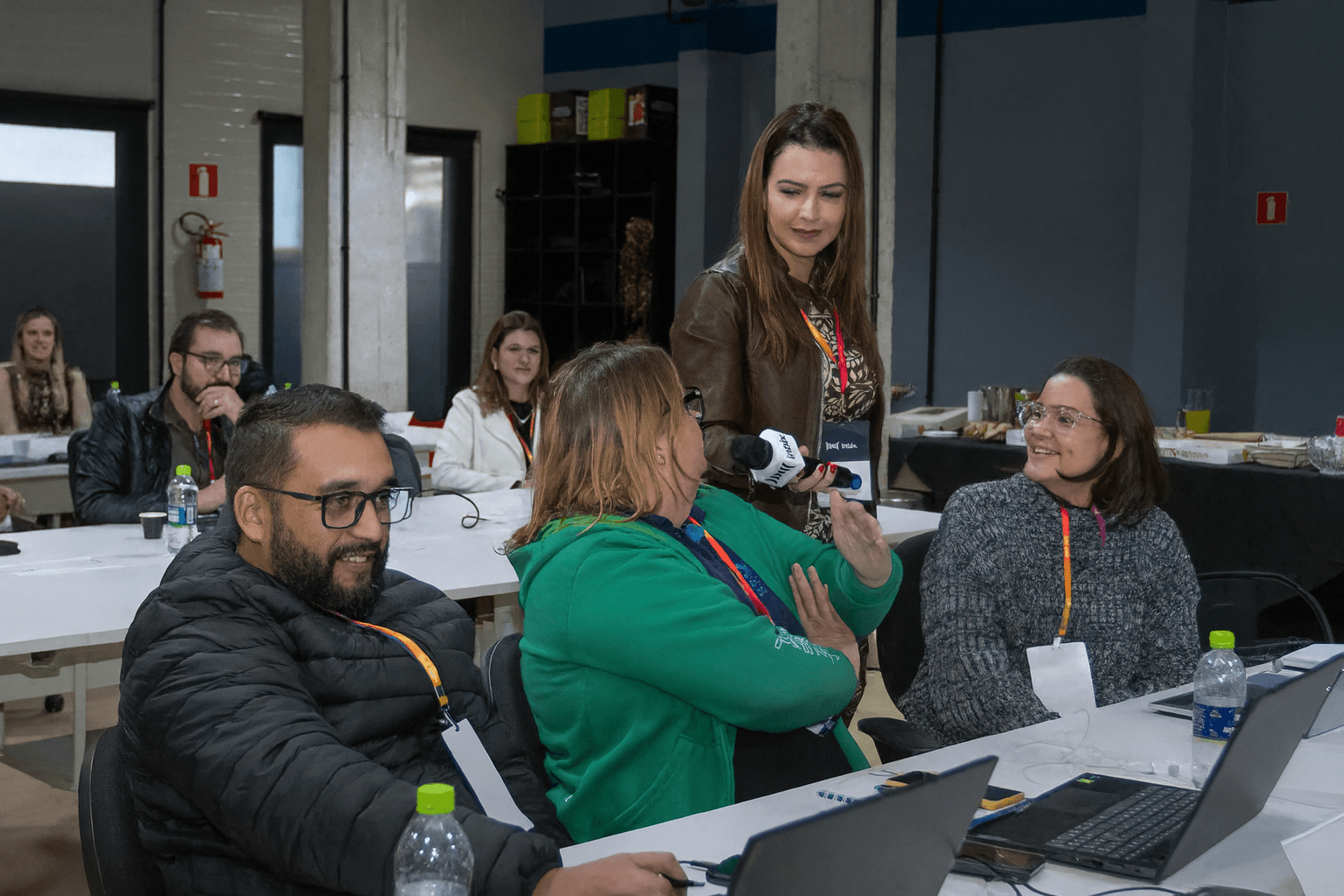 Facilitadora com microfone conduzindo dinâmica entre os participantes sentados