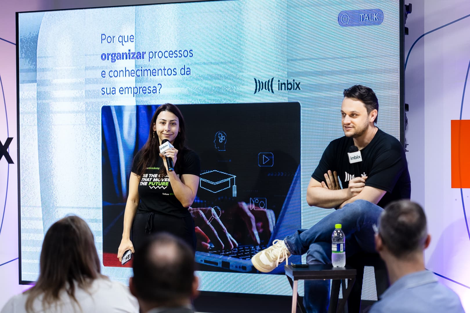 Palestrantes no palco com o slide Por que organizar processos e conhecimentos da sua empresa