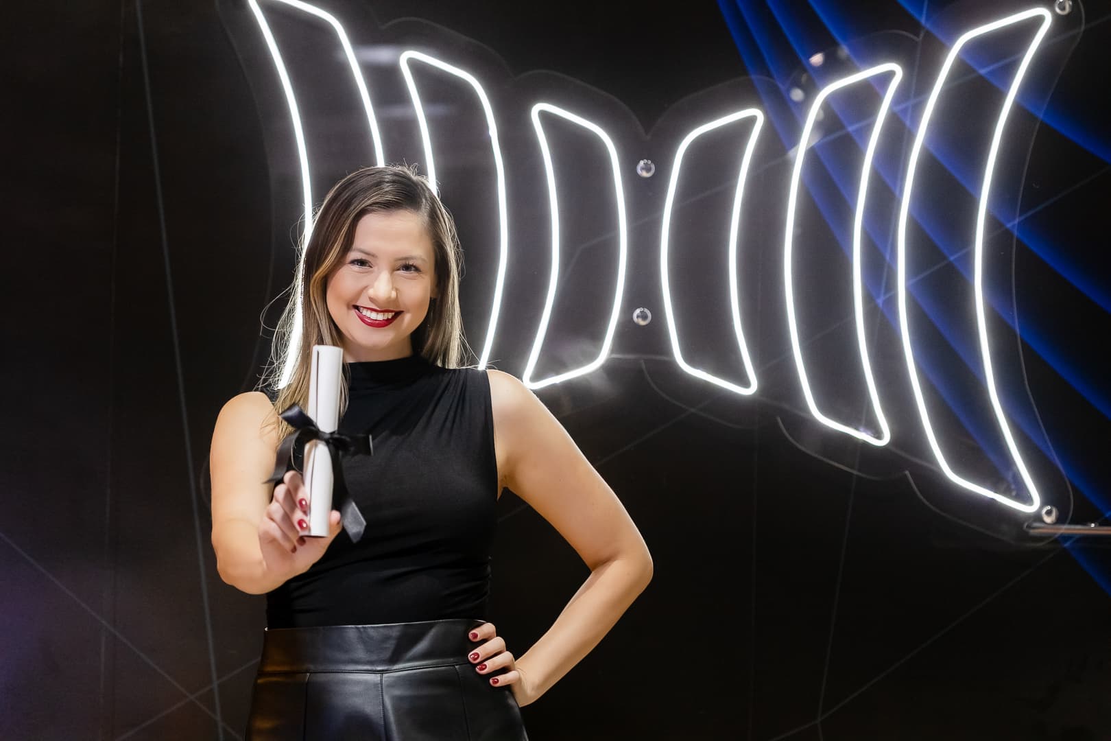Participante sorrindo com o diploma em mãos diante do painel luminoso da Inbix